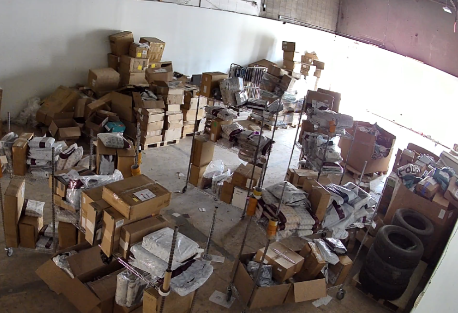 Warehouse sorting area with scattered packages, boxes, shopping carts and items awaiting processing